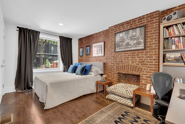 bedroom with wood finished floors, brick wall, a brick fireplace, baseboards, and visible vents