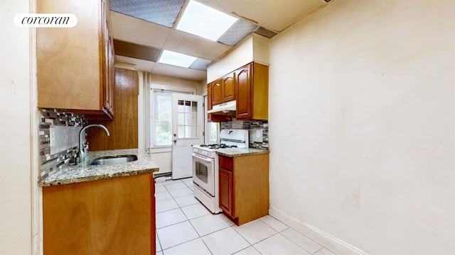 kitchen featuring light stone countertops, white range with gas cooktop, decorative backsplash, sink, and light tile patterned floors