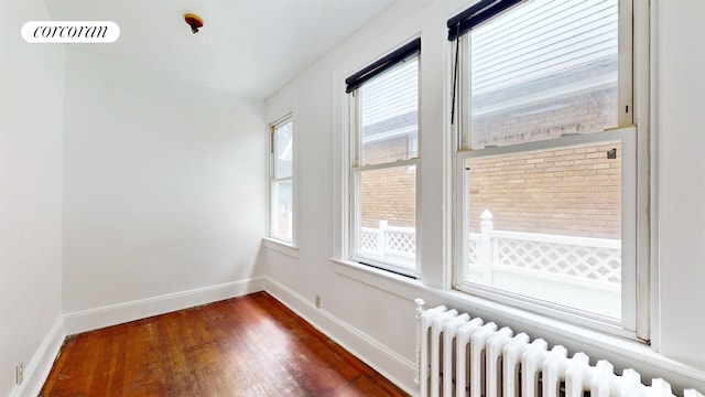 unfurnished room featuring radiator heating unit, wood finished floors, visible vents, and baseboards