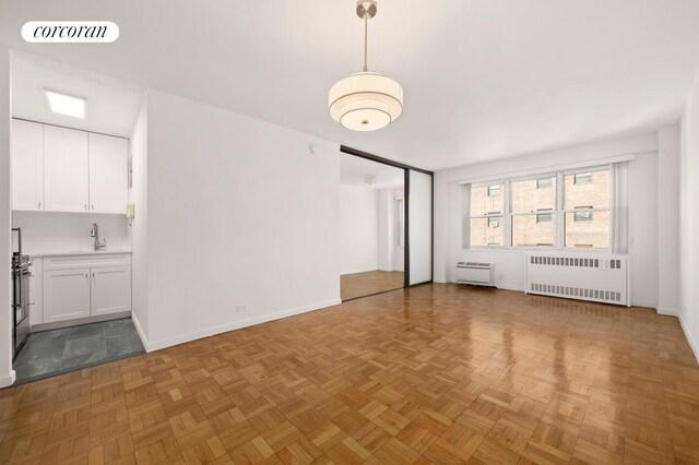 unfurnished living room featuring light parquet flooring, radiator, and sink