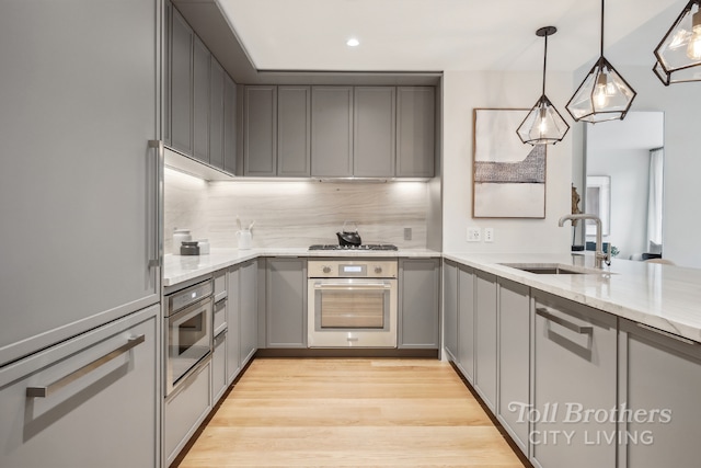 kitchen featuring light stone countertops, appliances with stainless steel finishes, sink, hanging light fixtures, and gray cabinets