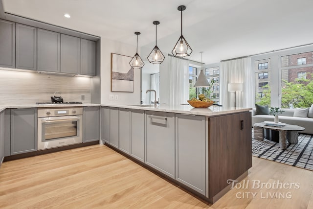 kitchen featuring light hardwood / wood-style floors, decorative backsplash, hanging light fixtures, gray cabinets, and stainless steel oven