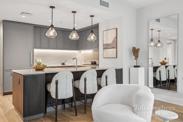 kitchen featuring a kitchen bar, light hardwood / wood-style floors, pendant lighting, and gray cabinets