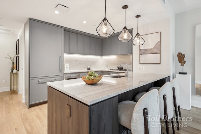 kitchen featuring kitchen peninsula, decorative light fixtures, light wood-type flooring, light stone counters, and a breakfast bar