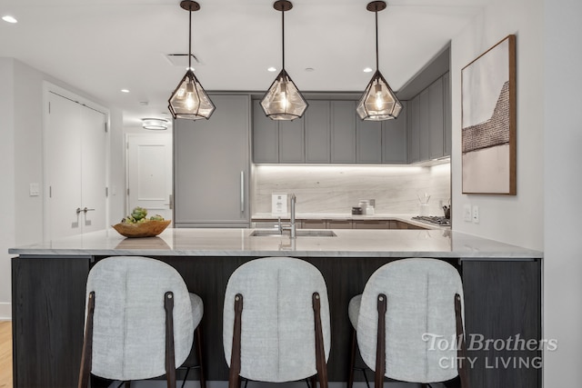 kitchen with decorative light fixtures, a breakfast bar, kitchen peninsula, sink, and gray cabinetry