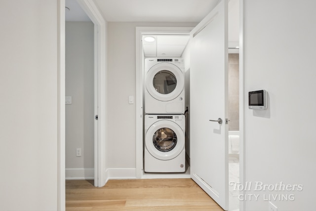 clothes washing area with stacked washer and clothes dryer and light wood-type flooring