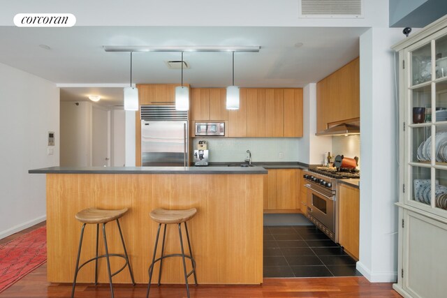 kitchen featuring hanging light fixtures, backsplash, a kitchen breakfast bar, a center island, and built in appliances