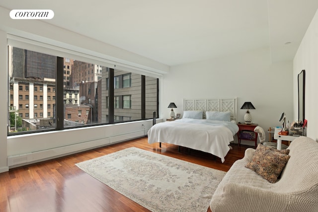 bedroom with a baseboard heating unit, wood finished floors, and visible vents