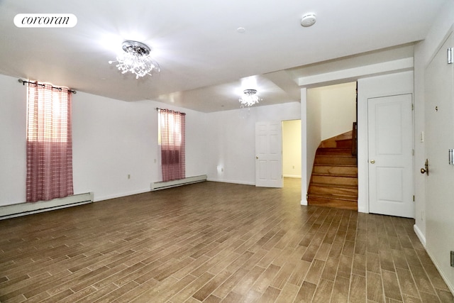 spare room featuring a baseboard heating unit, stairway, wood finished floors, and visible vents