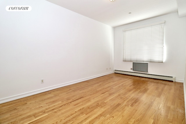 spare room with visible vents, a baseboard heating unit, baseboards, and wood finished floors