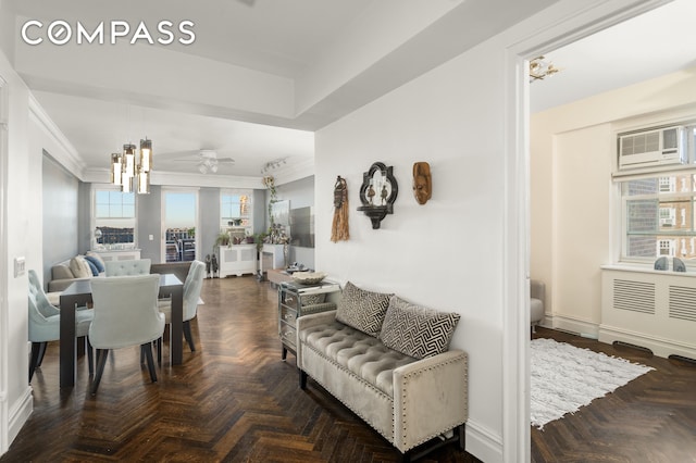 living room featuring ceiling fan with notable chandelier, a wall mounted AC, and crown molding