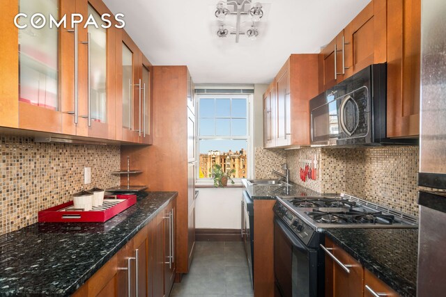 kitchen featuring black microwave, dark stone counters, range with gas stovetop, brown cabinetry, and a sink