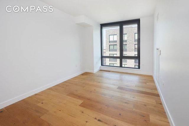 spare room with light wood-type flooring, visible vents, and baseboards