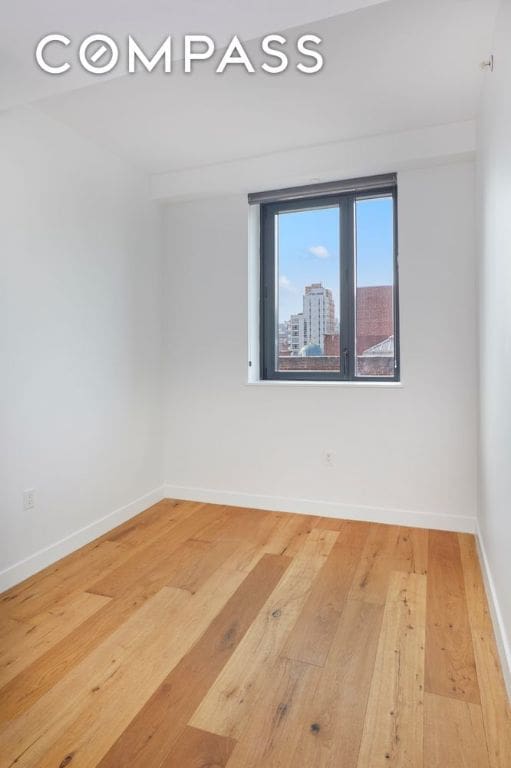 unfurnished room featuring a view of city, wood finished floors, and baseboards