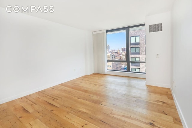 unfurnished room with light wood finished floors, baseboards, visible vents, a city view, and floor to ceiling windows