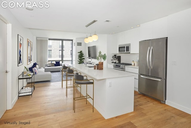 kitchen featuring appliances with stainless steel finishes, white cabinetry, hanging light fixtures, a kitchen island with sink, and light wood-type flooring