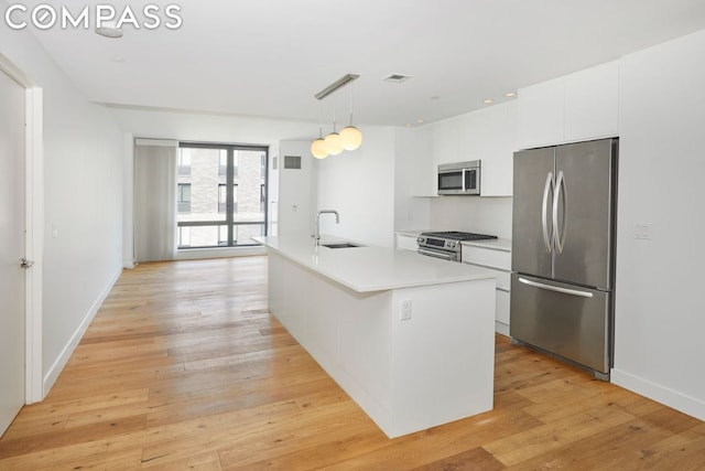 kitchen with a center island with sink, appliances with stainless steel finishes, hanging light fixtures, white cabinets, and sink