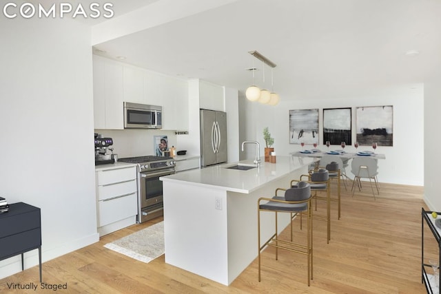 kitchen with white cabinetry, light hardwood / wood-style floors, stainless steel appliances, a kitchen island with sink, and hanging light fixtures