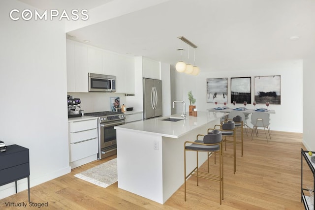 kitchen with white cabinets, appliances with stainless steel finishes, hanging light fixtures, a kitchen island with sink, and light countertops