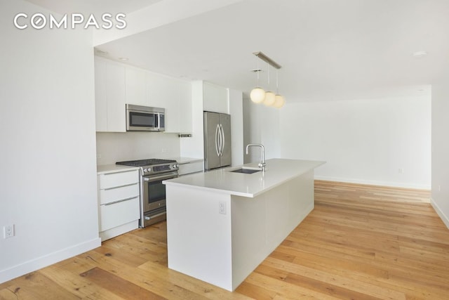 kitchen featuring a center island with sink, white cabinets, decorative light fixtures, stainless steel appliances, and light countertops