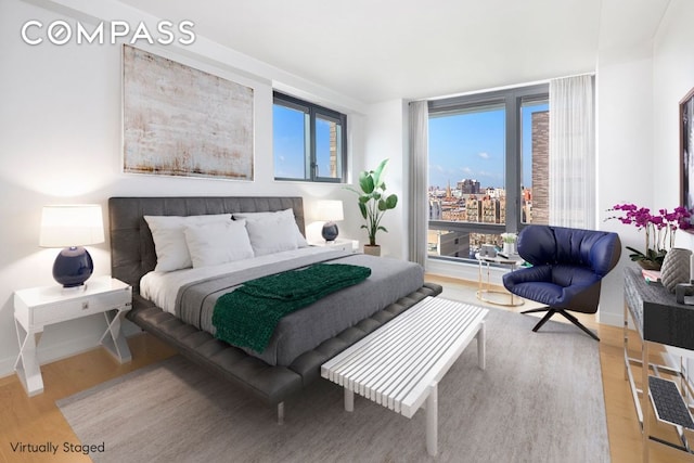 bedroom with a city view, light wood-style flooring, and baseboards