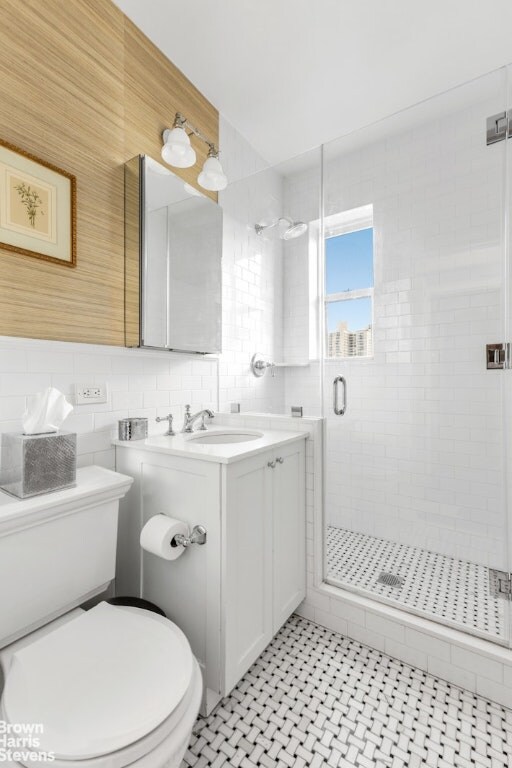 bathroom featuring toilet, a shower with door, tile walls, backsplash, and vanity