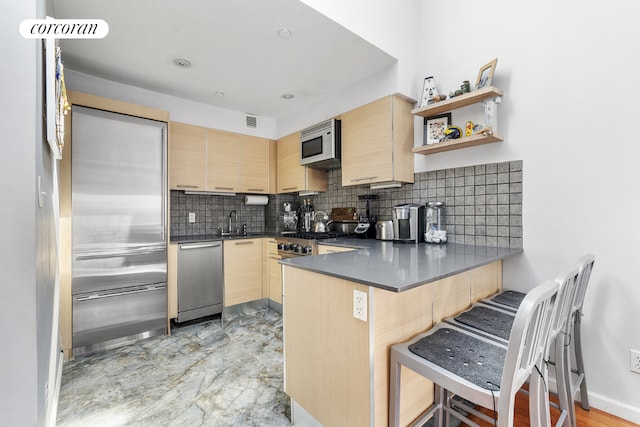 kitchen featuring a kitchen breakfast bar, light brown cabinets, stainless steel dishwasher, and kitchen peninsula