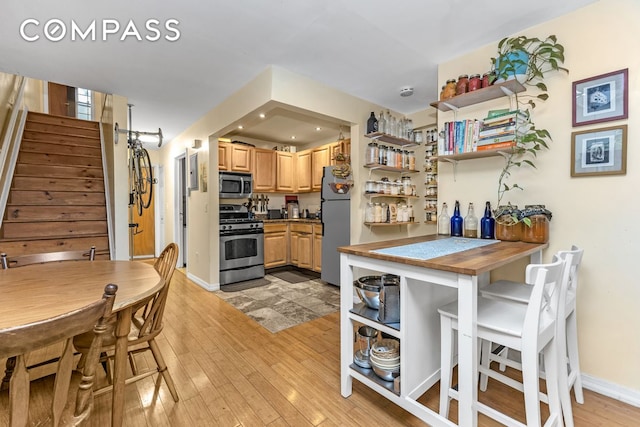 kitchen featuring light brown cabinets, light wood-style flooring, baseboards, appliances with stainless steel finishes, and open shelves