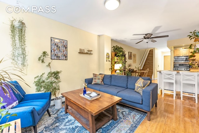 living room featuring light wood-type flooring, ceiling fan, and stairs