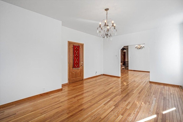 empty room with light wood-type flooring and a notable chandelier