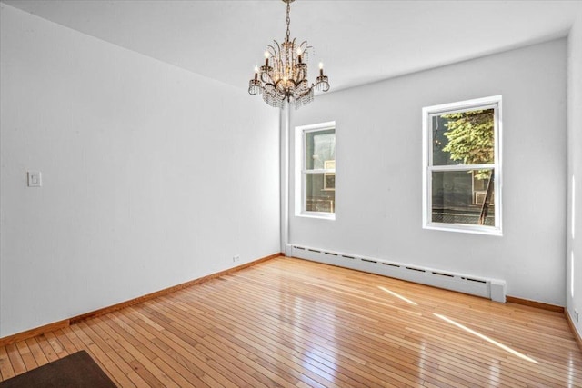 empty room featuring a chandelier, a baseboard heating unit, and light hardwood / wood-style floors