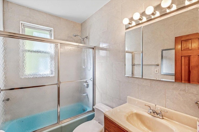 full bathroom featuring toilet, tile walls, shower / bath combination with glass door, vanity, and backsplash