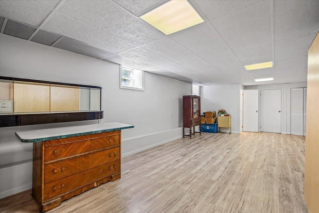 basement with a paneled ceiling and light hardwood / wood-style flooring