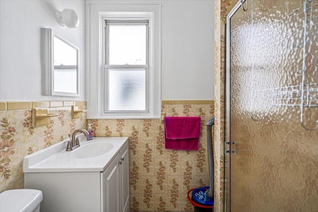 bathroom with toilet, tile walls, a shower with shower door, and vanity