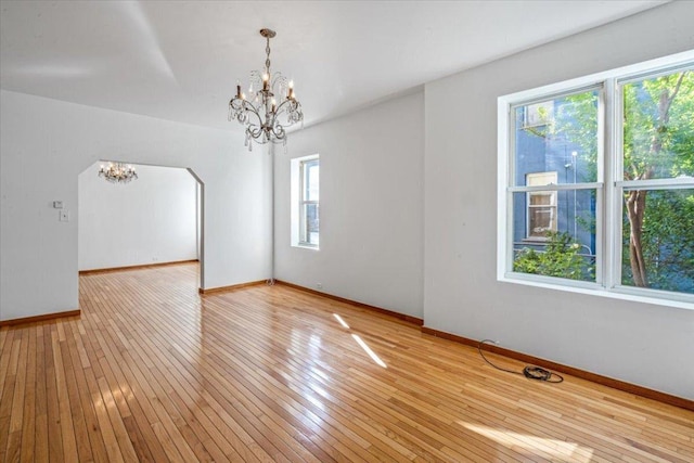 spare room with plenty of natural light, a notable chandelier, and light hardwood / wood-style floors