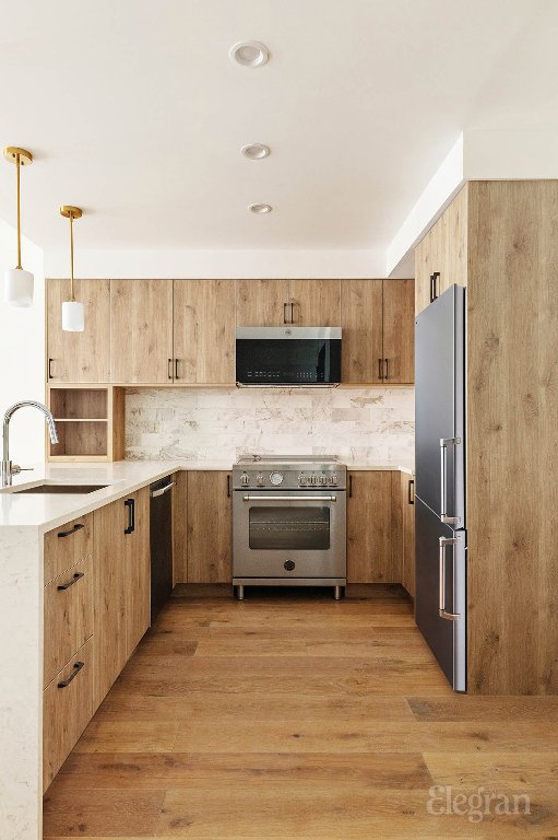 kitchen featuring decorative light fixtures, tasteful backsplash, light hardwood / wood-style floors, sink, and high end appliances