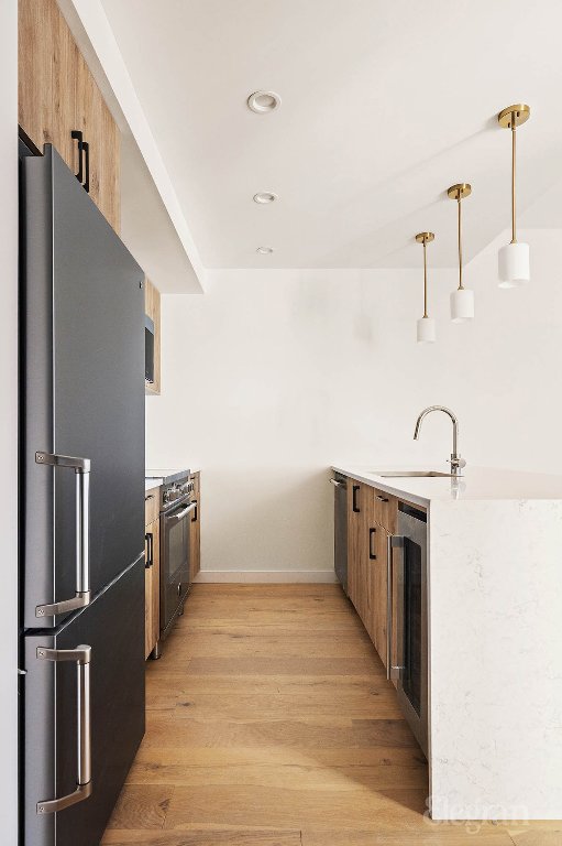 kitchen with high end appliances, pendant lighting, light wood-type flooring, and sink