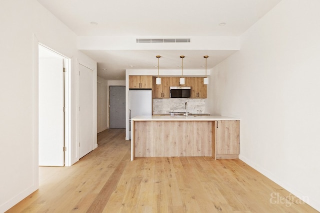 kitchen with appliances with stainless steel finishes, decorative backsplash, light hardwood / wood-style floors, hanging light fixtures, and kitchen peninsula