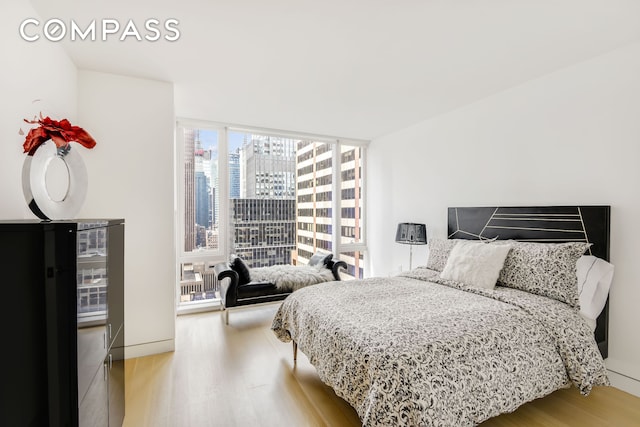 135 W 52nd St Unit 23C, New York City, NY 10019 - bedroom featuring floor to ceiling windows, wood finished floors, a view of city, and baseboards