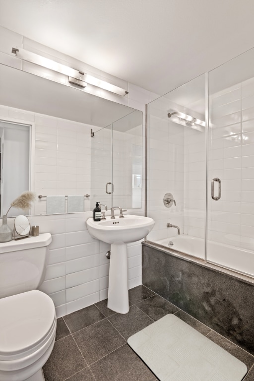 bathroom with toilet, combined bath / shower with glass door, tile walls, and tile patterned floors