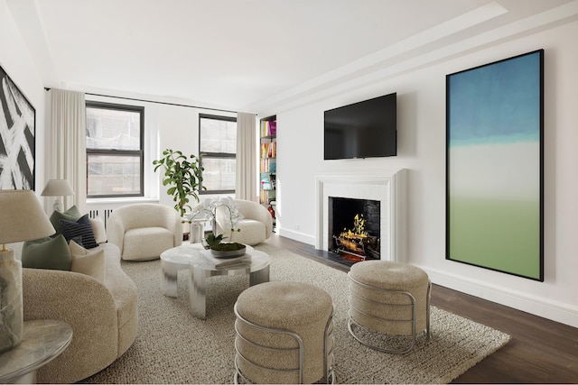 living area featuring a fireplace with flush hearth, baseboards, and wood finished floors