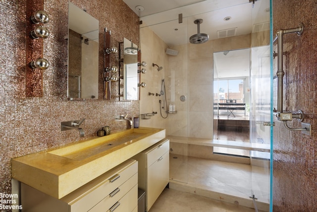 bathroom with a shower with shower door, tile walls, backsplash, vanity, and tile patterned floors