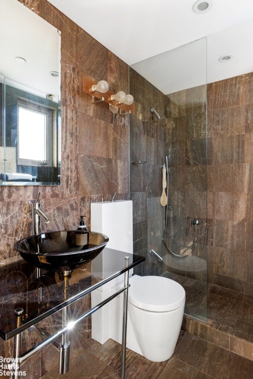 bathroom featuring a tile shower, sink, tile walls, and toilet