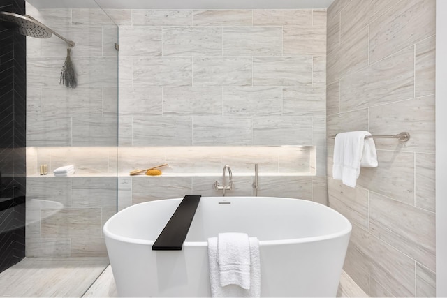 bathroom with tiled shower, a soaking tub, and tile walls