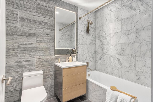 full bathroom with vanity, a combined bath / shower with marble appearance, toilet, and tile walls