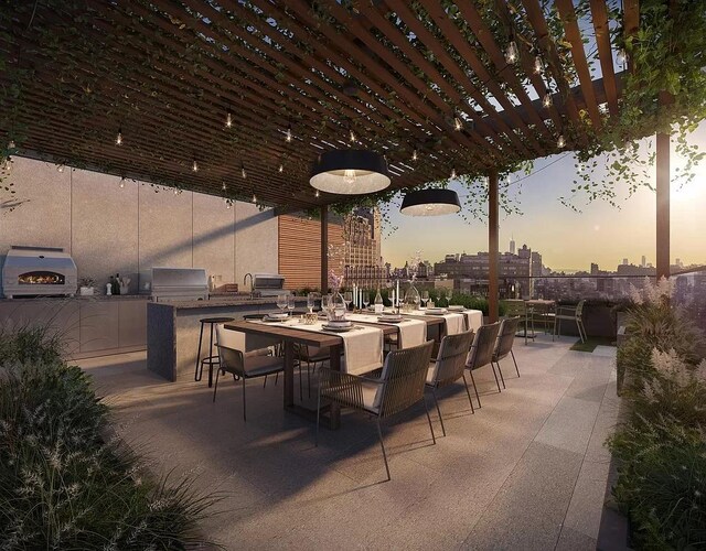 patio terrace at dusk featuring a pergola, exterior kitchen, grilling area, and outdoor dining space