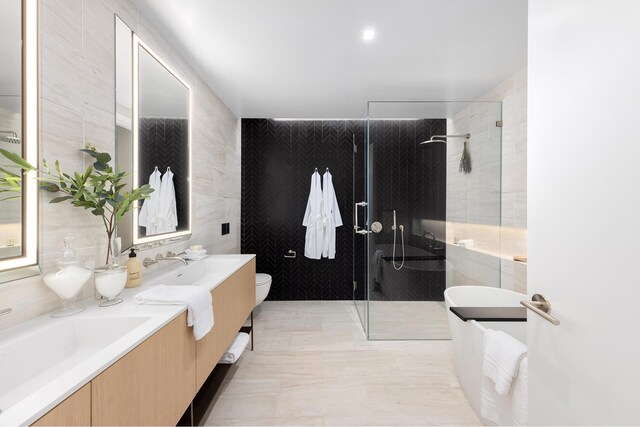 full bathroom with double vanity, toilet, tile walls, a shower stall, and a sink