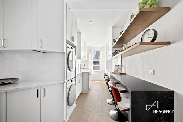 kitchen featuring stacked washer / drying machine, fridge, sink, light hardwood / wood-style flooring, and white cabinets