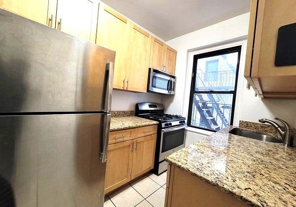 kitchen featuring light tile patterned flooring, stainless steel appliances, light stone counters, and sink