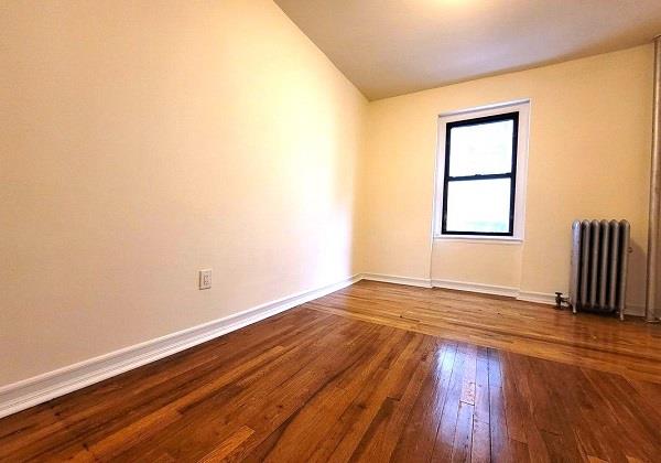 unfurnished room featuring lofted ceiling, radiator, and wood-type flooring